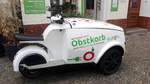 Seitenansicht eines dreirädrigen Motorrollers mit Lastenbox vorne als Transporter für Obstkörbe.