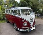 VW T1 Achtsitzer Sondermodell aus dem Jahr 1964. Ab dem Modelljahr 1963 wurde dieses Modell mit den flachen vorderen Blinkern, im Volksmund auch  Samba  genannt, angeboten. Mit der Einf�hrung des VW T2a im Jahr 1967 viel das Sondermodell weg. Die Sonderausstattung bestand aus der Dachrandverglasung, auch Oberlichter genannt, den verchromten Alu-Zierleisten, dem gro�en Faltschiebedach und einer Zeituhr im Inneren des Fahrzeuges. Der gesichtete  Samba  ist zus�tzlich mit verchromten Exportsto�stangen, aufklappbaren  Tropen-Windschutzscheiben  und geschmiedeten  Fuchs-Felgen  vom Porsche 911 ausgestattet. Der im Heck verbaute, Gebl�se-gek�hlte, Vierzylinderboxermotor hat serienm��ig einen Hubraum von 1.493 cm� und leistet 42 PS. Besucherparkplatz eines Restaurants in Essen-Kettwig am 12.07.2026.