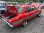 Profilansicht eines Ford Escort MK1 RS2000. Im Vereinigten Königreich kam der von den dortigen Ford-Werken als Nachfolger des  Anglia  entwickelte Escort im Januar 1968 auf den Markt. Nahezu unverändert wurde er ab September 1968 in das Verkaufsprogramm der deutschen Ford-Werke übernommen. Montiert wurde der deutsche Escort anfänglich nur im belgischen Werk Genk, später aber auch im Werk Saarlouis. Der größte Teil der Produktion ging ins Ausland, da der Escort auf dem deutschen Markt wegen seiner pummeligen Form, seiner holprigen Straßenlage und seines bescheidenen Komforts nur mäßigen Zuspruch fand. Ab Mai 1973 stand dann das sportliche Spitzenmodell RS2000 bei den Händlern. Insgesamt wurden rund 4000 Autos dieses Typs produziert. 2000 im britischen Werk Dagenham und 2000 im Werk Saarlouis. Ein solcher Escort war 1973 ab DM 10.400,00 zu bekommen. Serienmäßig hat dieses Modell einen Vierzylinderreihenmotor mit einem Hubraum von 1993 cm³ und einer Leistung von 100 PS. Classic car meeting am 13.07.2024 in Blaenavon/South-Wales. 