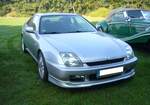Honda Prelude der Baureihe BB in der Version 2.2 VTI. Die Baureihe BB ist somit die fünfte Generation des Sport-Coupes Honda Prelude. Die Baureihe kam 1997 auf den Markt und wurde in Deutschland bis ins Jahr 2000 verkauft. In anderen Ländern erfolgte der Verkauf noch bis Sommer 2002. Das Modell war mit zwei Motorisierungen lieferbar. Der gezeigte Prelude ist mit dem stärkeren, lieferbaren, Motor ausgerüstet. Dieser Vierzylinderreihenmotor hat einen Hubraum von 2157 cm³ und leistet genau 200 PS. Gegen Aufpreis konnte das Modell mit der vom Vorgänger bekannten, elektronisch gesteuerten, elektrisch betätigten Vierradlenkung bestellt werden. Oldtimertreffen auf dem Gelände des Bikertreffs Mutter Vogel in Marl am 28.09.2025.