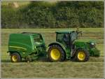 Am 16.07.2013 war dieser John Deere Traktor auf einem Feld mit einer Rundballenpresse im Einsatz das auf Reihen gelegte Heu zusammenzupressen.