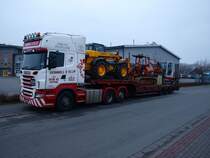 Ein Scania V8 R580 mit 3achsigen Auflieger. Beladen ist der Auflieger mit groen Baumaschinen, Anbaugerten, Baggerschaufeln und einer Palette Pflastersteine.  