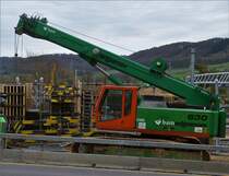 Sennebogen 630, Raupenkran steht an der Brückenbaustelle über die Eisenbahn in Ettelbrück, geschützt vor dem Straßenverkehr von einer Baustellen Leitplanke. 02.2020
