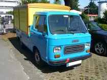 Fiat 900E mit einem Pritschenaufbau der Carrozzeria Coriasco/Turin. Der Kleintransporter 900E kam 1979, als Weiterentwicklung des bereits im Jahr 1970 erschienenen Fiat 850T auf den Markt. Angetrieben wurde dieser Lieferwagen vom, im Heck verbauten, Motor des Fiat 127. Dieser Motor hat einen Hubraum von 903 cm³ und leistet 35 PS. Die Höchstgeschwindigkeit gab das Werk mit 100 km/h an. An dem roten Streifen auf der vorderen Stoßstange kann man erkennen, dass dieser Fiat früher in Italien unterwegs war. Der rote Streifen bedeutet, dass mit dem Auto nur Produkte der eigenen Firma transportiert wurden. Mülheim an der Ruhr Saarn am 25.07.2021.
