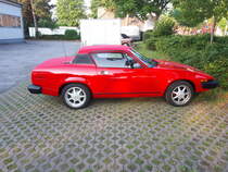 Profilansicht eines Triumph TR7 Coupes im Farbton pimento red. Kundenparkplatz einer Autowerkstatt in Mülheim an der Ruhr.