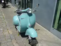 Vespa 150 Super aus dem Jahr 1962. Genau wie die Ur-Vespa 98 aus dem Hause Piaggio, hat die Vespa 150 einen Pressstahlrahmen mit integrierter Frontverkleidung, Der Einzylinderzweitaktmotor hat einen Hubraum von 145,5 cm³ und leistet in der 150 Super 5,5 PS. Diese Motorleistung reicht um den Roller auf eine Höchstgeschwindigkeit von 85 km/h zu beschleunigen. Parkplatz der Düsseldorfer Classic Remise am 12.07.2022.