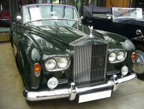 Rolls Royce Silver Cloud III Convertible aus dem Jahr 1964. Produziert wurde dieses Modell t von 1962 bis 1965. Als der Silver Cloud III im Jahr 1962 vorgestellt wurde, fiel dem Fachpublikum als erstes der Wechsel zu Doppelscheinwerfern und eine niedriger geführte Linie der vorderen Kotflügel und der Motorhaube auf. Zum ersten Mal konnte auch das Chassis des Rolls-Royce für den Aufbau einer Coupé- oder Cabriolet-Varianten bestellt werden, die bis dato exklusiv dem fast baugleichen Bentley Continental vorbehalten war. Der V8-Motor hat einen Hubraum von 6230 cm³ und leistet 187 PS. Dieser, im Farbton velvet green lackierte Silver Cloud III wurde 1964 gebaut und ist einer von nur 25 produzierten, linksgelenkten Silver Cloud III Convertible. Ein Vorbesitzer dieses Fahrzeuges ist der US-amerikanische Schauspieler Nicolas Cage. Classic Remise Düsseldorf am 30.12.2022.