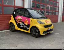 Gelb - Schwarzer Smart mit Werbung abgestellt in Worben vor einem Garage am 10.06.2023