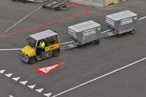 Kleiner Schlepper unterwegs mit 2 Koffercontainer auf dem Flughafen von Wien. 06.2023