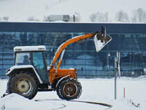 Ein mir unbekannter orangefarbener Traktor überquert gerade einen Bahnübergang, so gesehen Ende November 2023 in Pfronten.