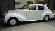 Profilansicht eines Bentley R-Type Sports Saloon aus dem Jahr 1952. Die Baureihe R-Type war kein wirklich neues Auto, sondern ein modernisierter Bentley MK VI. Er hatte allerdings einen größeren Kofferraum als sein Vorgänger und die Motorhaube war zweiflügelig zu öffnen. Außerdem war serienmäßig eine heizbare Heckscheibe verbaut. Ab dem Jahr 1953 hielt eine in Lizenz von General Motors hergestellte Viergangautomatic (drei Gänge plus Overdrive) Einzug. Zunächst nur für die Exportmodelle, ab 1954 auch für die Heimatmarktmodelle. Vom R-Type wurden insgesamt wurden bis 1955 2.320 Fahrzeuge dieses Typs mit den verschiedensten Karosserieaufbauten produziert. Der Sechszylinderreihenmotor hat einen Hubraum von 4566 cm³ mit einer Leistung von ca. 150 PS. Classic Remise Düsseldorf am 26.02.2024.