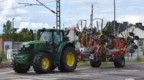 Ein JOHN DEERE 6195 M Traktor mit Vierkreiselschwader mit Mittenablage vom Hersteller PÖTTINGER Typ TOP 1252 C als Hänger am 12.06.24 Bahnübergang Bahnhof Rodleben.