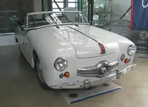 Panhard Dyna Junior X. In der unmittelbaren Nachkriegszeit gab es überall in Europa, also auch in Frankreich, Materialbeschränkungen. Dies war in allen Industriezweigen bis weit in die 1950`er Jahre spürbar. Während einige Hersteller der Automobilindustrie bei der Materialbelieferung Vorrang hatten, wie beispielsweise Renault, das mit seinem 4CV als erster Hersteller voll einsatzfähig war, mussten andere Hersteller warten und meist ihre überarbeiteten Vorkriegsfahrzeuge anbieten. In dieser tristen Automobillandschaft stach Panhard mit seinem Dyna X in seinem unverwechselbaren Stil und der Aluminiumkarosserie hervor. Von 1951 bis 1956 wurde auf dieser Basis ein hübscher, kleiner Roadster, der gezeigte Dyna Junior, gebaut. Ab 1954 wurde der vom Dyna X übernommene Kühlergrill mit der Kugel in der Mitte verbaut. In diesem Jahr wird die Version mit den vier Stuer-PS (4CV) eingestellt, so das nur noch das Cabrio im Handel bleibt. Der Zweizylinderboxermotor hat einen Hubraum von 851 cm³ und leistet 42 PS. Darüber hinaus kann das Modell mit einem MAG-Kompressor geordert werden. Mit dieser Option erhöht sich die Leistung auf 60 PS. Diese Motorleistung ist gut für eine Höchstgeschwindigkeit von rund 145 km/h. Classic Remise Düsseldorf am 09.06.2025.