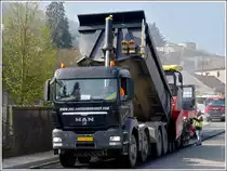 Strassenbauarbeiten in Wiltz. Der MAN Lkw hat sich vor den Asphaltfertiger gesetzt, hebt den Kipper und bef�llt so den hungrigen Rachen des Asphaltfertigers. 13.04.2012 